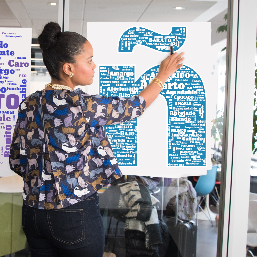 A teacher using a large printed word cloud poster with Spanish adjectives as a teaching tool
