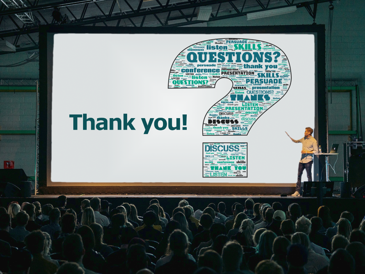 A picture of a conference room with many people, the presenter standing in front of a very large screen, and the presentation slide reads "Thank you! Questions?" as a word cloud